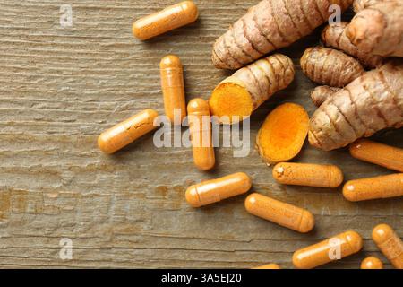 Capsules de curcuma en cuillère et racines sur table en bois, pose à plat. Espace pour le texte Banque D'Images