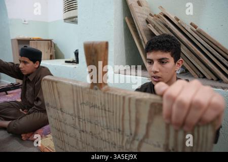 Misrata, Libye. 23 mars 2025. Un étudiant se concentre sur la lecture de versets du Saint Coran écrits sur sa tablette en bois, les enfants libyens sont assis dans une école coranique traditionnelle, inscrivant soigneusement des versets sur des tablettes en bois pendant que leur professeur les guide dans la récitation. Cette méthode séculaire, ravivée pendant le Ramadan, reste une pratique chère pour mémoriser le Saint Coran. (Photo par Islam Alatrash/SOPA images/SIPA USA) crédit : Sipa USA/Alamy Live News Banque D'Images
