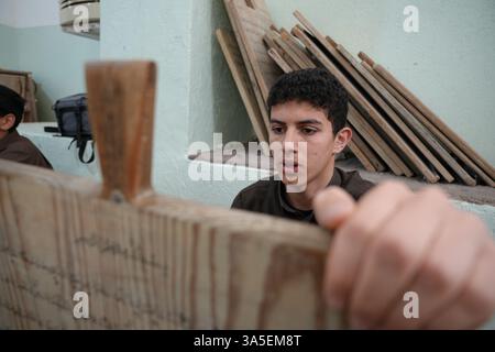 Misrata, Libye. 23 mars 2025. Un étudiant se concentre sur la lecture de versets du Saint Coran écrits sur sa tablette en bois, les enfants libyens sont assis dans une école coranique traditionnelle, inscrivant soigneusement des versets sur des tablettes en bois pendant que leur professeur les guide dans la récitation. Cette méthode séculaire, ravivée pendant le Ramadan, reste une pratique chère pour mémoriser le Saint Coran. Crédit : SOPA images Limited/Alamy Live News Banque D'Images