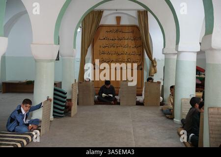 Misrata, Libye. 23 mars 2025. Un étudiant se concentre sur la lecture de versets du Saint Coran écrits sur sa tablette en bois, les enfants libyens sont assis dans une école coranique traditionnelle, inscrivant soigneusement des versets sur des tablettes en bois pendant que leur professeur les guide dans la récitation. Cette méthode séculaire, ravivée pendant le Ramadan, reste une pratique chère pour mémoriser le Saint Coran. (Photo par Islam Alatrash/SOPA images/SIPA USA) crédit : Sipa USA/Alamy Live News Banque D'Images