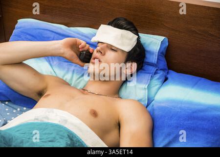 Beau jeune homme malade ou pas bien au lit avec une grippe ou une fièvre médecin appelant au téléphone Banque D'Images