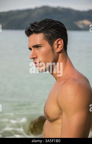 Jeune homme attrayant dans la mer sortant de l'eau avec les cheveux mouillés, regardant loin d'un côté. Vue profil Banque D'Images