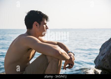 Beau jeune homme de la mer sortir de l'eau avec les cheveux mouillés, regardant au loin, vue de profil Banque D'Images