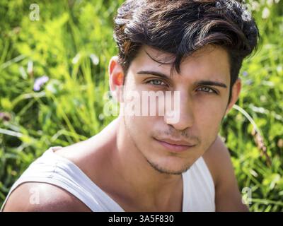 Photo de la tête d'un beau jeune homme aux yeux verts en plein air, regardant la caméra devant les prairies Banque D'Images