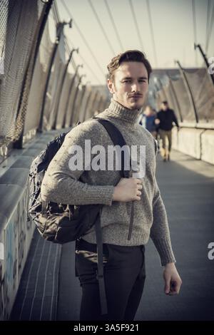 Beau jeune homme de la ville à pied avec sac à dos sur une épaule, portant des vêtements d'hiver Banque D'Images