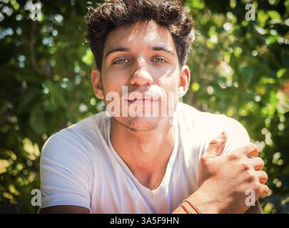 Photo de tête d'un beau jeune homme aux yeux verts en plein air, regardant la caméra devant des plantes et des prairies Banque D'Images