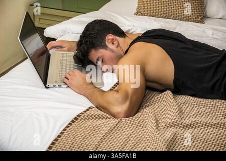 Close Up of assez jeune homme aux cheveux noirs de dormir sur le plancher à côté d'un ordinateur portable avec la main sur le clavier Banque D'Images