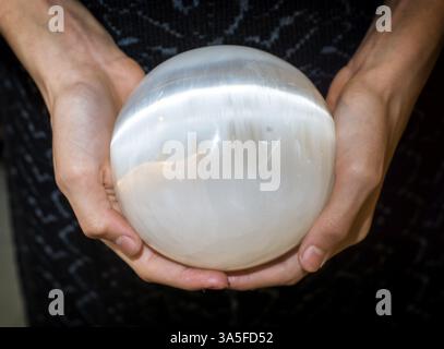 Gros plan de mains féminines de culture tenant une sphère en sélénite ou en quartz blanc Banque D'Images