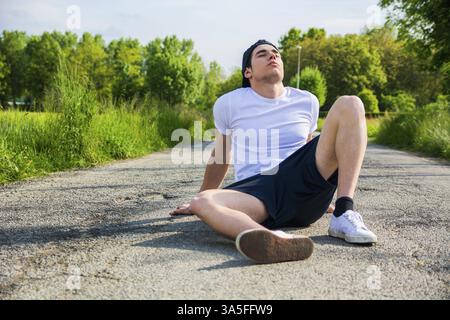 Beau jeune homme assis au repos sur la route après l'exécution et de jogging dans les pays d'une journée ensoleillée Banque D'Images