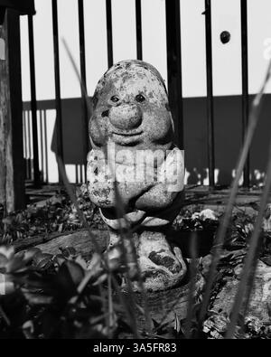Statue de gnome en pierre avec fond barré – photographie en noir et blanc Banque D'Images