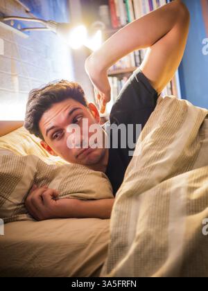 Jeune beau homme endormi, allongé dans le lit bâillant pendant qu'il se réveille Banque D'Images