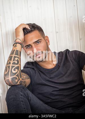 Beau jeune homme aux yeux verts se relaxant à la maison assis sur son canapé, regardant la caméra Banque D'Images