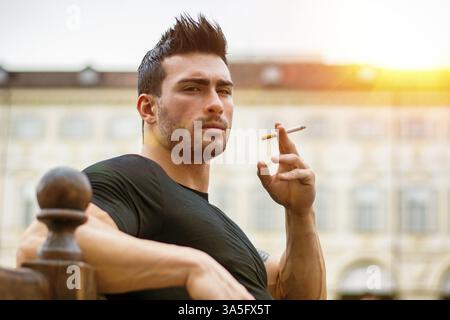 Bel homme masculin adulte regardant la caméra en étant assis et fumant Banque D'Images