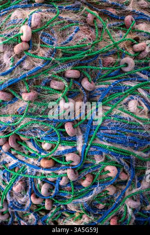Pile verticale de filets de pêche verts et bleus avec flotteurs bruns et textures altérées, capturés en détail. Banque D'Images