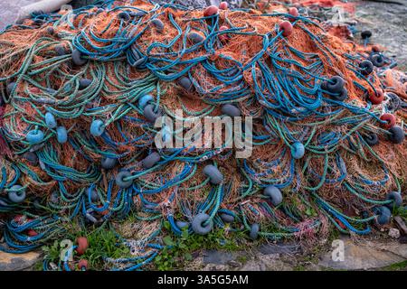 Pile de filets de pêche enchevêtrés avec des cordes bleues, vertes et oranges et des flotteurs sombres, reposant sur le sol à l'extérieur. Banque D'Images