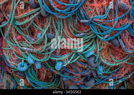 Gros plan de filets de pêche enchevêtrés avec des cordes vertes, bleues et oranges, des flotteurs noirs et des lests en plomb, montrant des détails complexes. Banque D'Images