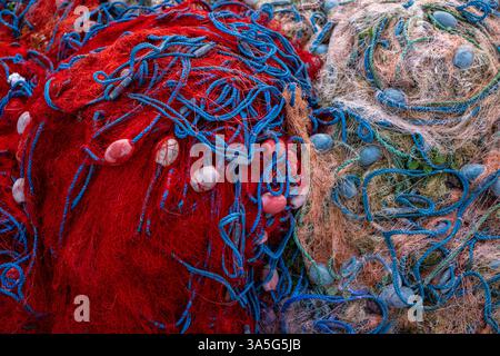 Deux piles de filets de pêche dans des tons rouge vif et beige doux avec des cordes et des flotteurs bleus, montrant contraste et texture. Banque D'Images