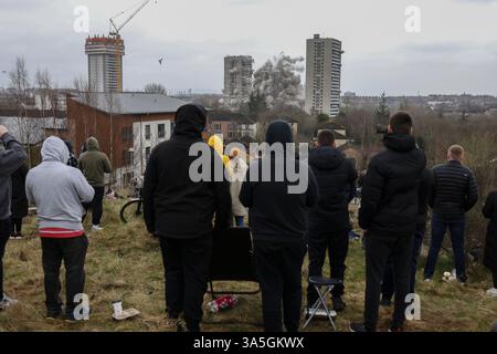 Glasgow, Royaume-Uni, 23 mars 2025. Les gens regardent la démolition contrôlée de trois immeubles de 26 étages sur le domaine de Wyndford, détruits pour faire place à de nouveaux logements abordables et un centre communautaire, à Maryhill, à Glasgow, en Écosse, le 23 mars 2025. Photo : Jeremy Sutton-Hibbert/Alamy Live News. Banque D'Images
