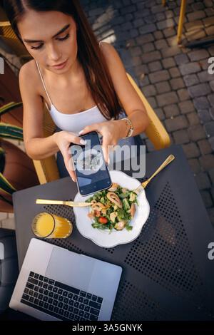 Faire une photo de nourriture. Belle jeune femme est à l'extérieur du restaurant près de la table. Banque D'Images