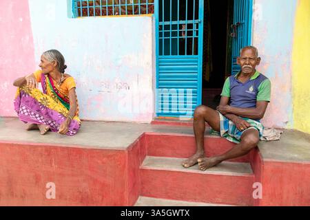 Femme portant des vêtements traditionnels indiens colorés sari assis devant une entrée d'une maison avec son mari, gunupur, orissa, inde Banque D'Images