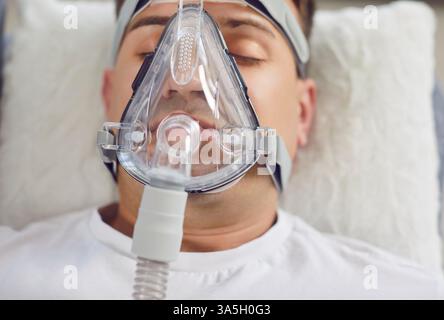 Gros plan Portrait d'un homme couché dans un lit d'hôpital respirant à travers un masque à oxygène Banque D'Images