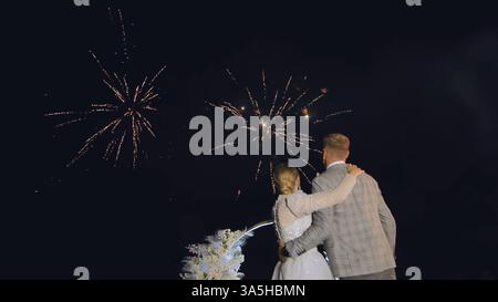 Couple de jeunes mariés s'embrassant sous des feux d'artifice éblouissants, partageant un moment intime de nuit de noces sous un ciel étoilé célébrant l'amour Banque D'Images