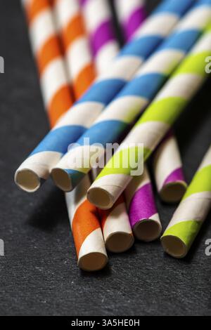Pailles de boisson multicolores sur fond de pierre sombre. Couleurs éclatantes contrastant sur lumière naturelle. Pailles en papier. Gros plan macro Banque D'Images