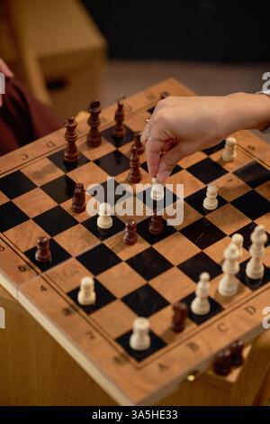 Gros plan des mains déplaçant des pièces sur un échiquier en bois pendant un match en intérieur. Les pièces d'échecs dispersées autour du plateau montrent la stratégie de jeu en cours de déroulement Banque D'Images