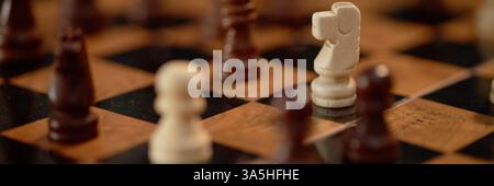 Plan d'en-tête du site Web d'un chevalier blanc et d'autres pièces d'échecs en bois disposées sur échiquier démontrant un positionnement complexe pendant le jeu Banque D'Images