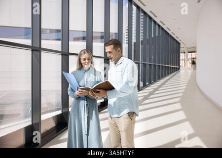 Deux professionnels debout dans le couloir contemporain regardant les dossiers de l'organisateur personnel, examinant des documents, se préparant pour la présentation, ou finalizi Banque D'Images