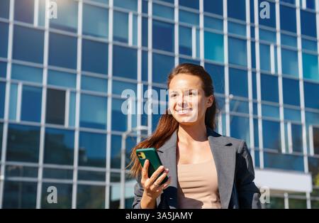 Femme urbaine réussie avec un téléphone portable dans sa main à l'extérieur sur la rue de la ville. Banque D'Images
