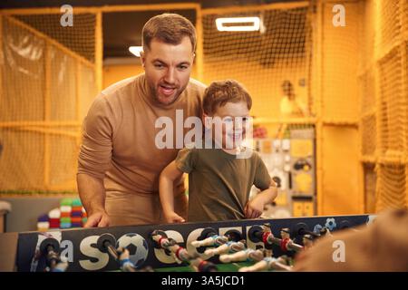 Amuse-toi bien. Famille de papa, mère et fils qui jouent à un jeu de baby-foot à l'intérieur. Banque D'Images
