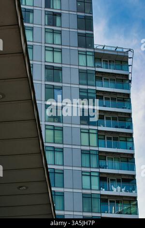 Vue partielle d'un grand bâtiment moderne avec balcons et nombreuses fenêtres, partiellement obscurcie par un surplomb en béton. Ciel bleu visible à Manchester, Royaume-Uni Banque D'Images