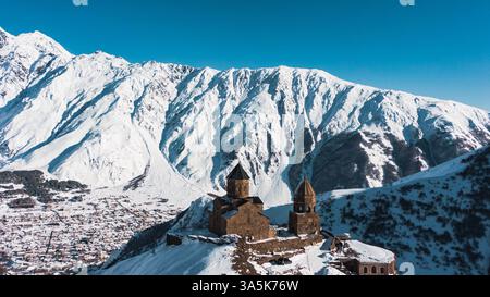 Gergeti trinity Church se trouve sur une colline surplombant la ville de stepantsminda et les imposantes montagnes du caucase enneigées au loin, créant une scène hivernale à couper le souffle en géorgie Banque D'Images
