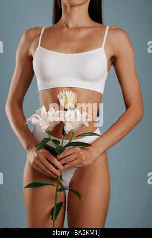 Montrer le corps et tenir des fleurs. La jeune femme est dans le studio en arrière-plan. Banque D'Images