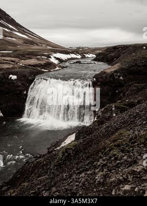 Cascade de Þórufoss en Islande, cascadant sur des falaises accidentées dans une rivière sinueuse. Les collines arides environnantes avec des taches de neige créent un spectaculaire Banque D'Images