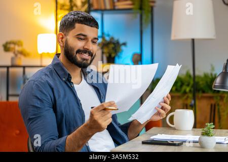 Homme barbu indien freelance travaillant avec des documents du bureau à domicile, analysant des informations, lisant des documents d'affaires préparent le rapport financier. Jeune homme hispanique comptable analysant des documents graphiques. Banque D'Images