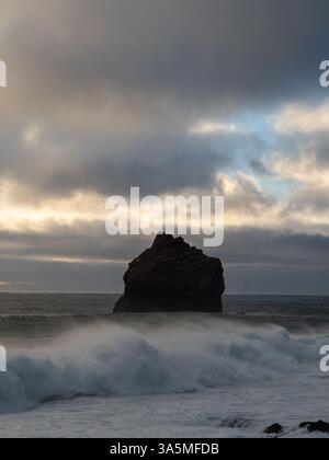 La mer sombre s'empilent au large de la côte islandaise de Valahnúkamöl au crépuscule, entourée de nuages spectaculaires et d'oiseaux marins survolant l'océan Atlantique Banque D'Images
