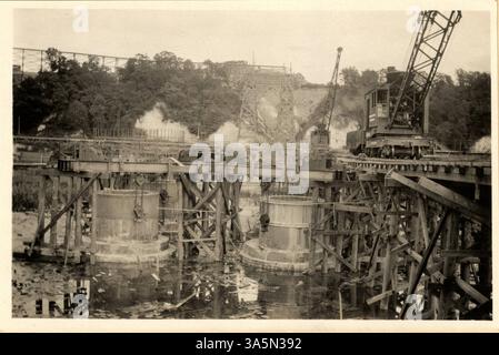 Cette image montre la base d'un quai en construction pour le pont Mendota. Des cylindres en béton sont utilisés pour former les fondations, tandis que des échafaudages en bois sont visibles en arrière-plan. Une voie ferrée est visible sur la gauche, utilisée pour le transport de matériaux de construction et de machines. Banque D'Images