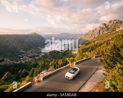 Monténégro, Kotor - 13 juillet 2024 : mariés et mariés conduisent dans un cabriolet blanc le long d'une route dans les montagnes au-dessus de la baie de Kotor. Monténégro Banque D'Images