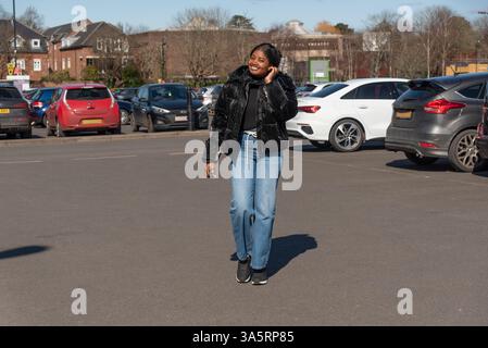 Chichester Angleterre Royaume-Uni. 18.03.2025. Femme habillée en veste noire et jeans wearimg marchant dans le parking. Banque D'Images