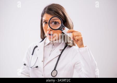 Studio a photographié le portrait d'une femme médecin inquiète qui regarde à travers une loupe. Banque D'Images