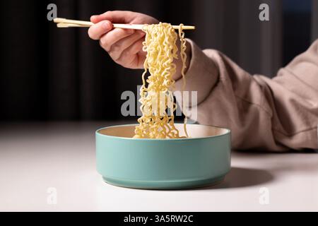 Femme mangeant des nouilles ramen avec des baguettes du bol à soupe à la maison. Mains prenant les nouilles du bol. Des aliments faits maison Banque D'Images