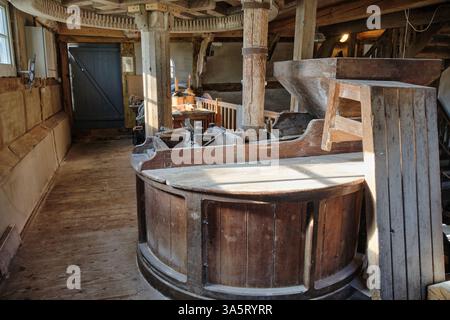 Meule traditionnelle encastrée dans du bois à l'intérieur d'un millésime historique. Les engrenages et les arbres en bois pilotent le processus de fraisage. La lumière du soleil met en évidence les faisceaux vieillissants et Banque D'Images