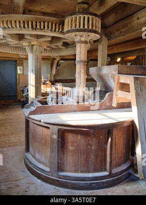 Meule traditionnelle encastrée dans du bois à l'intérieur d'un millésime historique. Les engrenages et les arbres en bois pilotent le processus de fraisage. La lumière du soleil met en évidence les faisceaux vieillissants et Banque D'Images