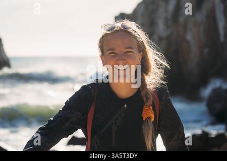 Femme souriant avec l'océan et les falaises derrière elle à Peniche. Banque D'Images