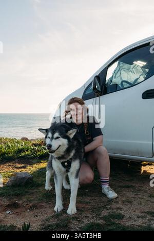 femme souriante avec husky à côté d'un camping-car au coucher du soleil Banque D'Images
