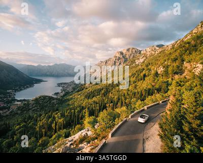 Monténégro, Kotor - 13 juillet 2024 : le cabriolet roule le long de l'autoroute de montagne au-dessus de la baie de Kotor. Monténégro. Drone Banque D'Images