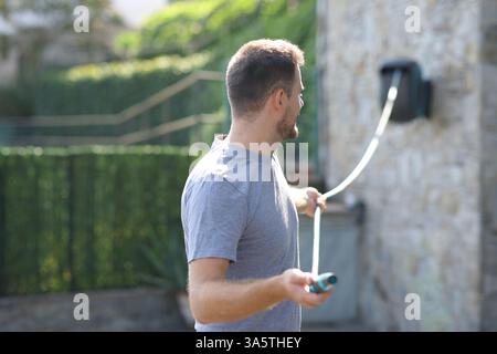 Homme debout dévidant tuyau dans un jardin dans un extérieur de maison Banque D'Images