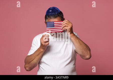 Un citoyen juif portant une kippa tient un drapeau américain et couvre son visage avec. Le concept de politique étrangère, de commonwealth et d'assistance. Banque D'Images
